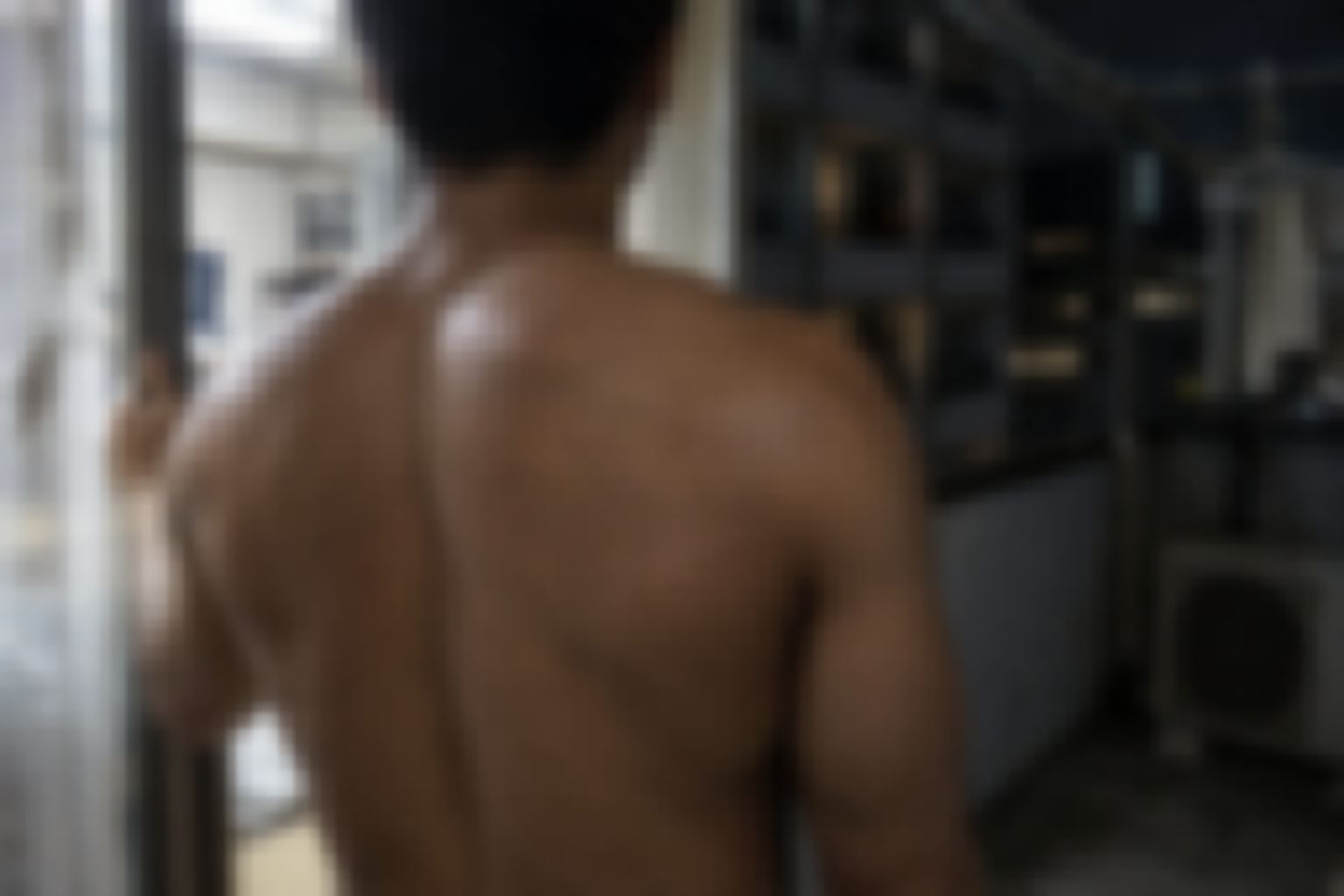 夜のアパートのベランダへサッシを開けて出ようとする、短髪で背中の広い男性の後ろ姿