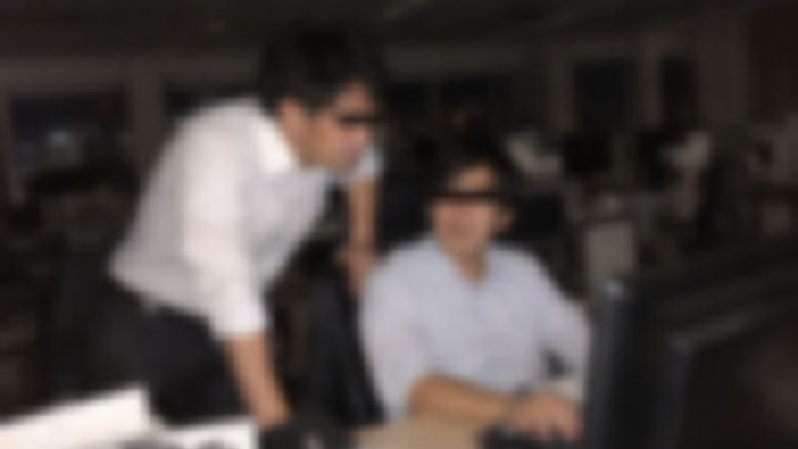 夜のオフィスで同僚の席に身を乗り出す男性