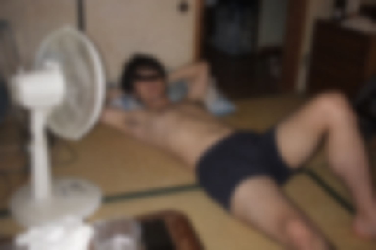 夏の畳の部屋で扇風機の前にボクサーパンツ姿で寝転ぶ男性