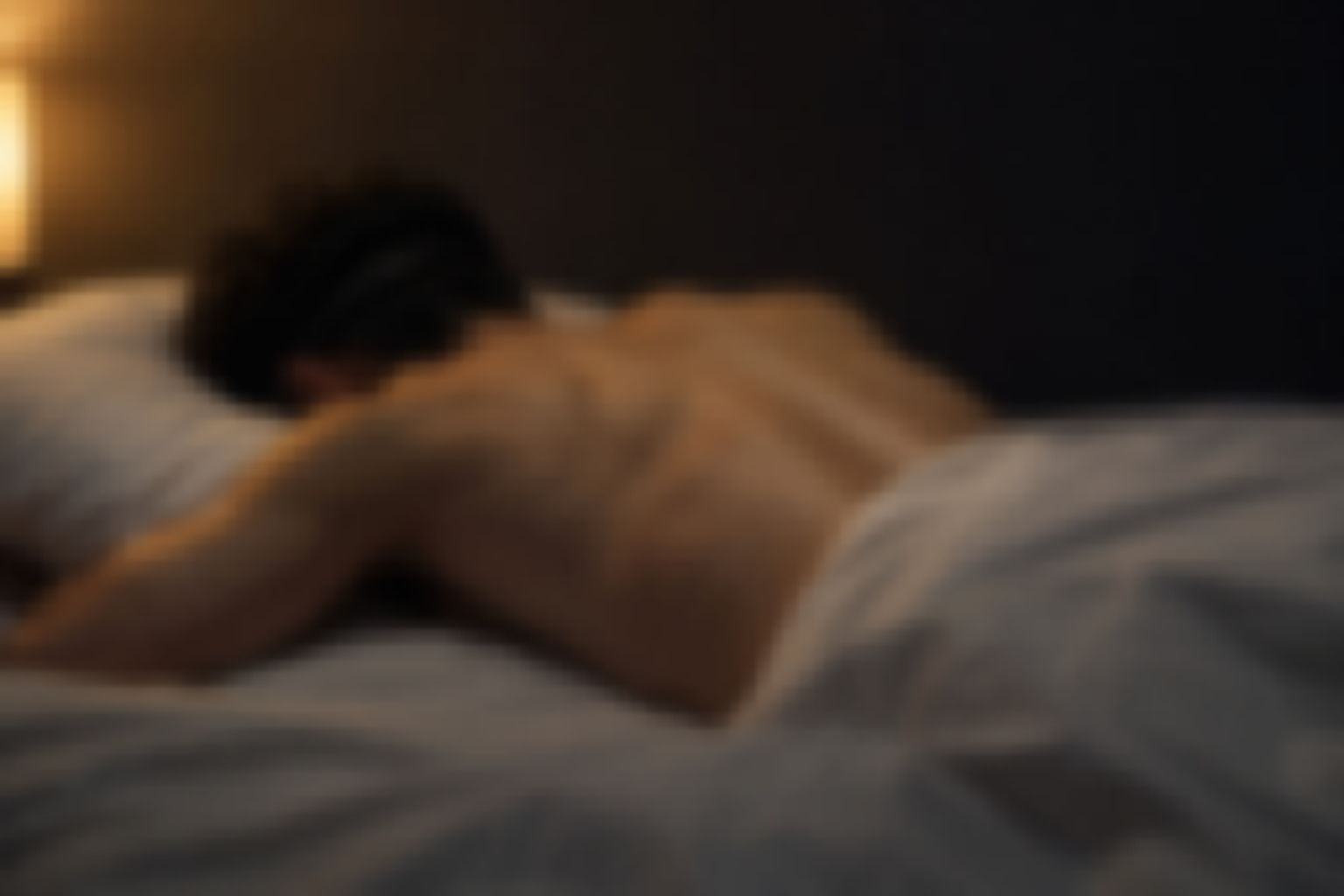 薄暗い部屋で、アイマスクをしたまま裸の背中でベッドにうつ伏せになる男性