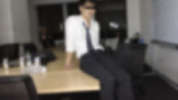 夜の会議室で机に腰かけるネクタイ姿の男性