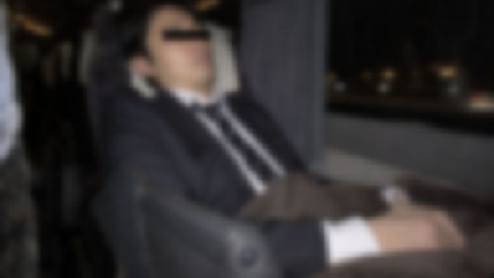夜行バスの座席で毛布をかけて眠るスーツの男性