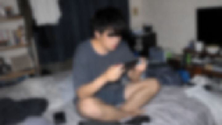 散らかった部屋のベッドで座ってゲームをする男性