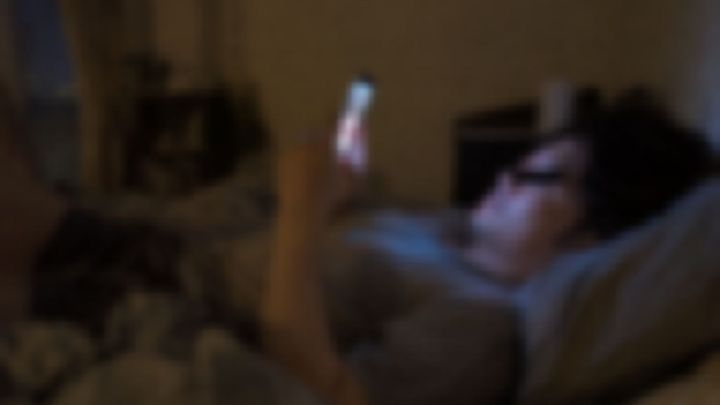 夜のベッドで横になってスマホを見る男性