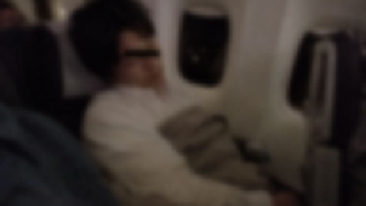 夜の機内で毛布をかけて眠るシャツ姿の男性