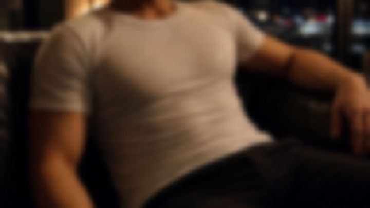 夜景を背にソファへ座る白いTシャツ姿の男性