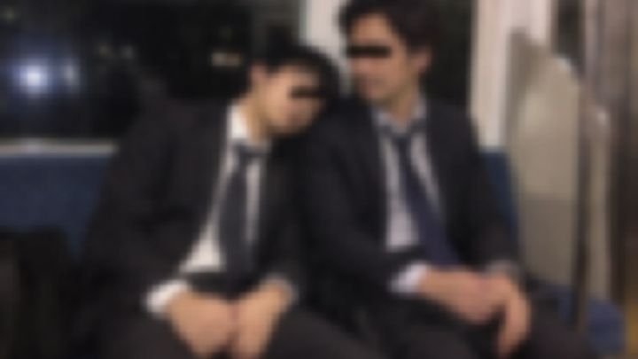 夜の電車で肩にもたれて眠るスーツの男性2人