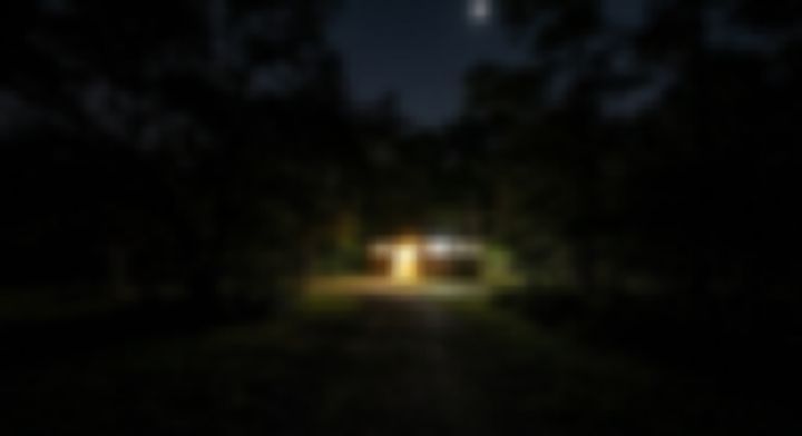 夜の木立の奥で明かりがともる小さな建物