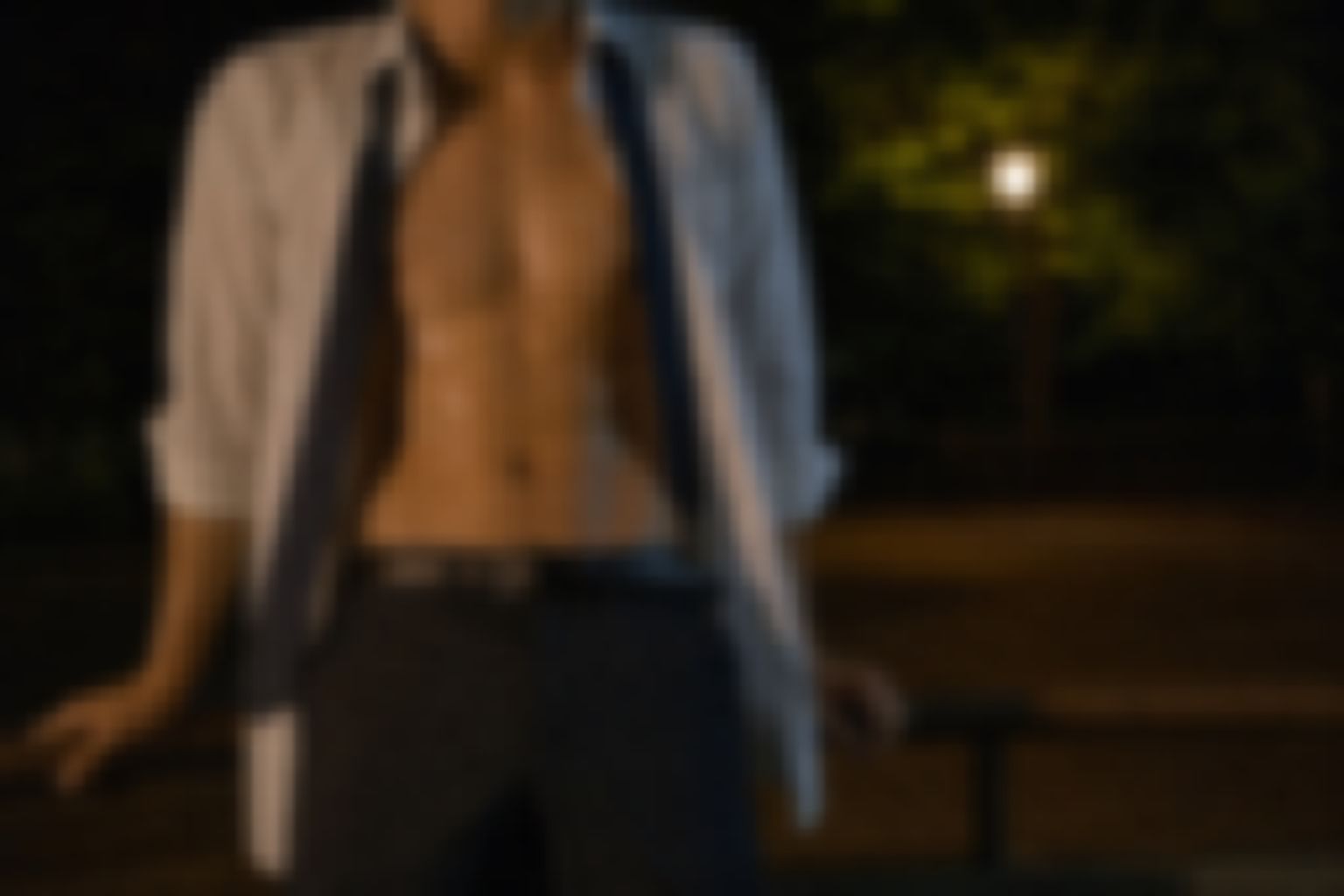 夜の公園で手すりにもたれる、白いシャツを開いた男性