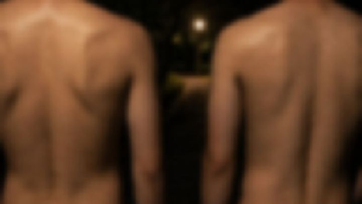 夜の公園で並んで立つ上半身裸の男性二人の後ろ姿