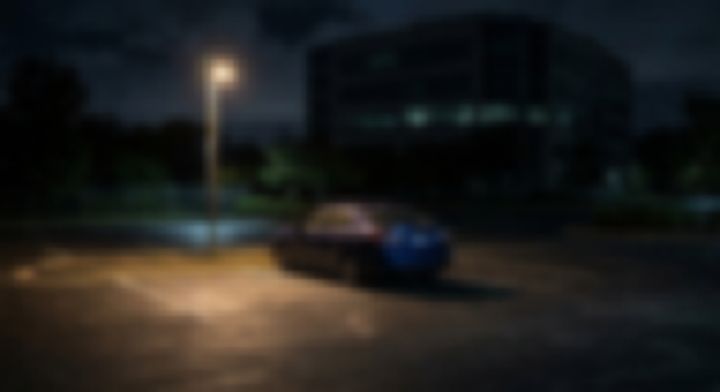夜のオフィスビル脇の駐車場に停まる一台の車