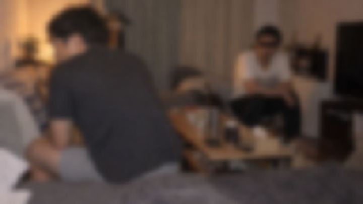 夜の部屋で背を向けて座る男性と、離れて座るもう1人